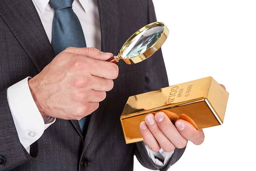 Business professional examining gold with magnifying glass, deciding to buy gold despite market conditions