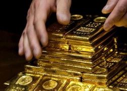 Hands carefully stacking several one kilo gold bars