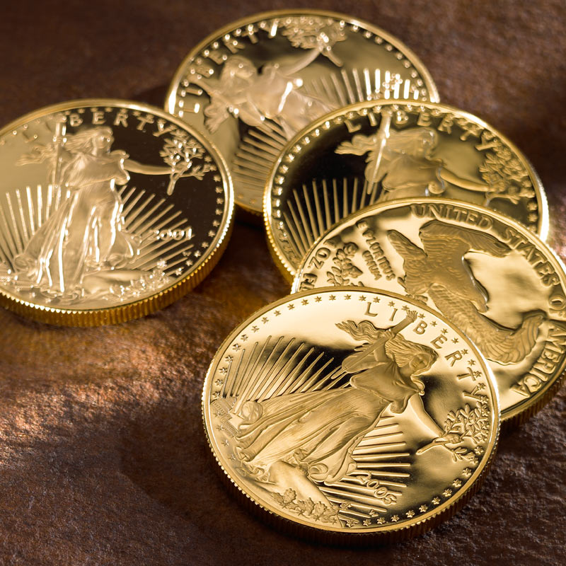 Five Gold American Eagle coins laying down on a table