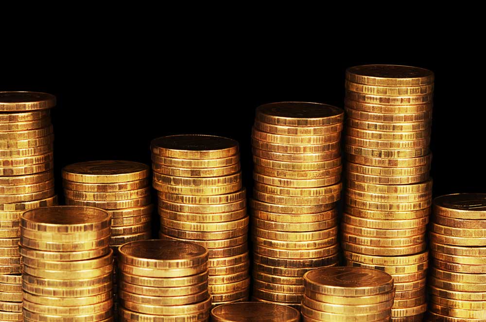 Various stacks of gold coins at different heights against pitch black background