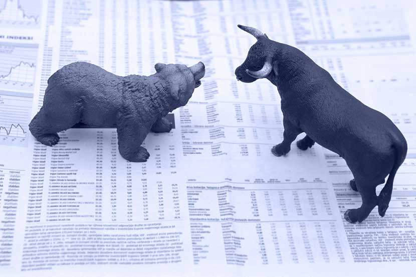 Bear and bull figurines standing off atop newspaper of stock market news
