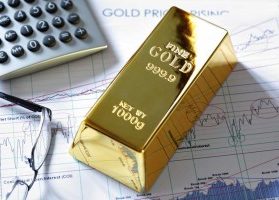 Fine gold bar sitting on stock market reports with calculator