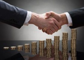 Two business men shaking hands over stacks of gold coins