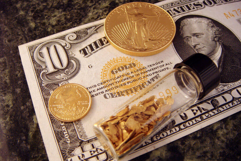 Gold coins, gold flakes in capsule, sitting on top of ten dollar bill