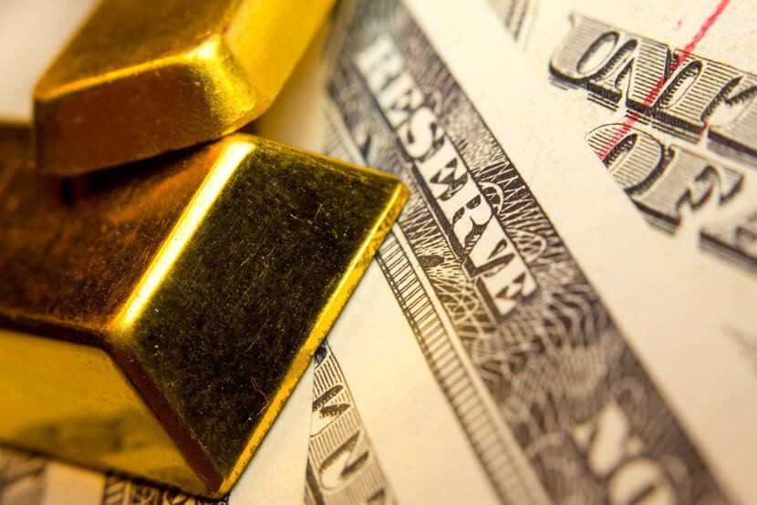 Two gold bars overlaid on top of U.S. currency, close up view of "Reserve"