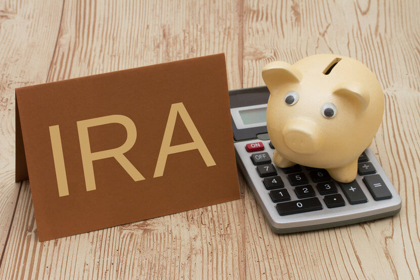 Gold piggy bank sitting on top of calculator and sign reading IRA