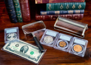 Gold and silver coins in protective slabs on wooden table with money and magnifying glass