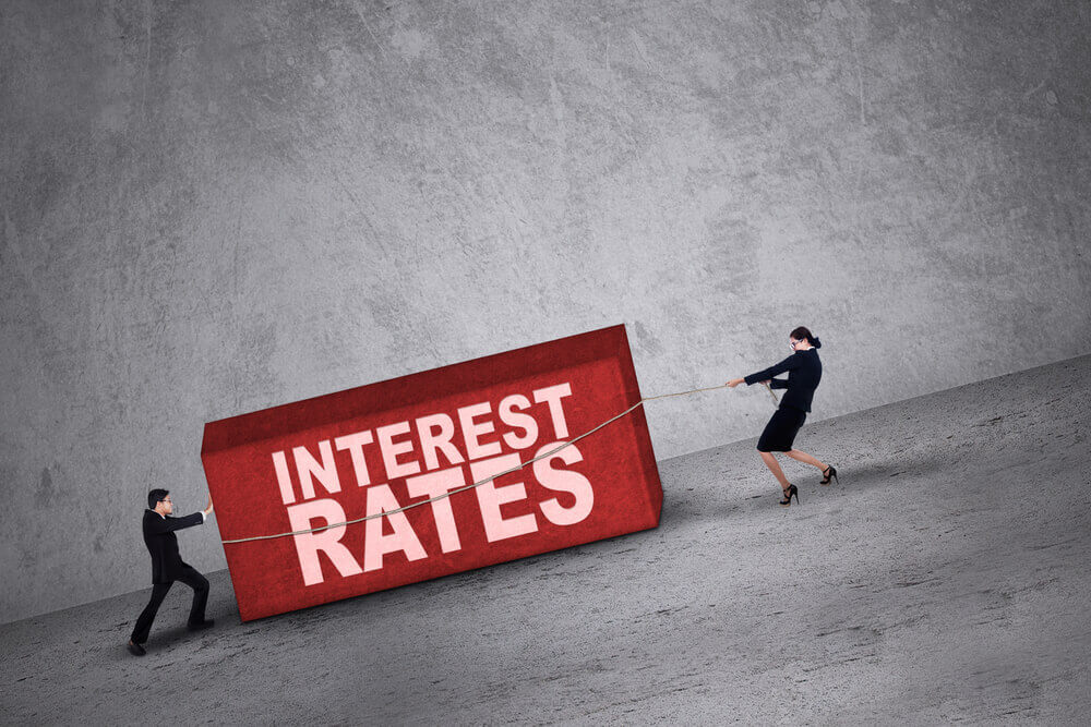 Businessman pushing and businesswoman pulling a block of Interest Rates uphill