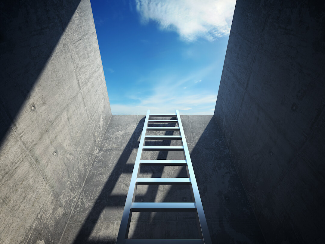 Perspective from inside a cement bunker with ladder in the middle showing a way out and blue sky in the background