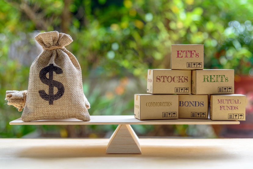 Dollar sacks on a wood bar balancing boxes with ETFs, stocks, REITs, commodities, bonds, and mutual funds