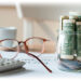 Glass jar containing cash next to glasses, calculator, and papers labeled “RETIREMENT PLAN”