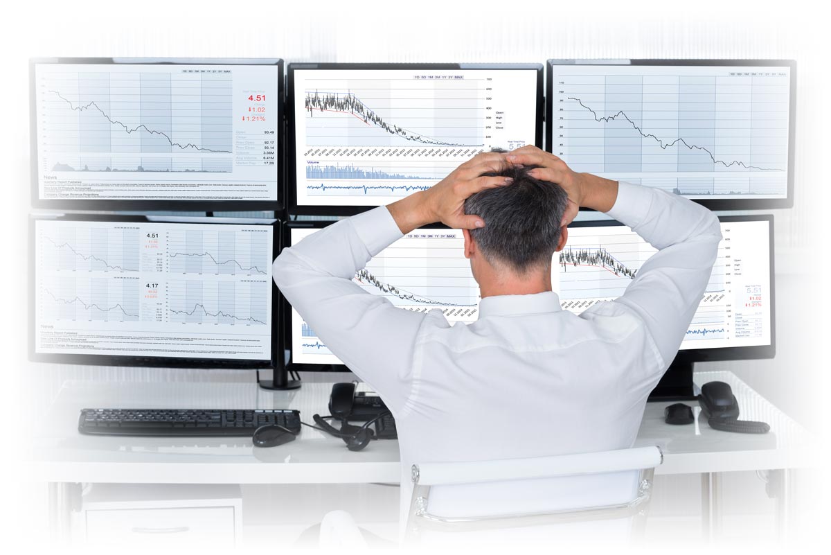 Analyst with hands on head as multiple monitors show negative-trending charts