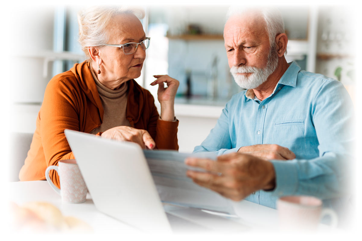 Older frustrated couple looking at documents and laptop