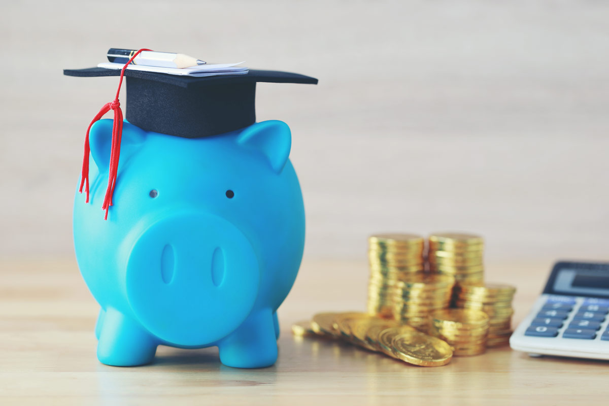 Blue piggy bank wearing graduation cap next to gold coins and calculator