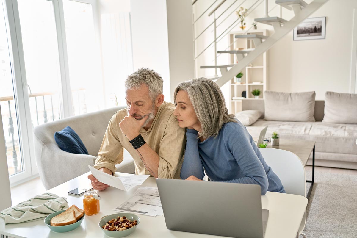 Retired couple looking over laptop and financial statements