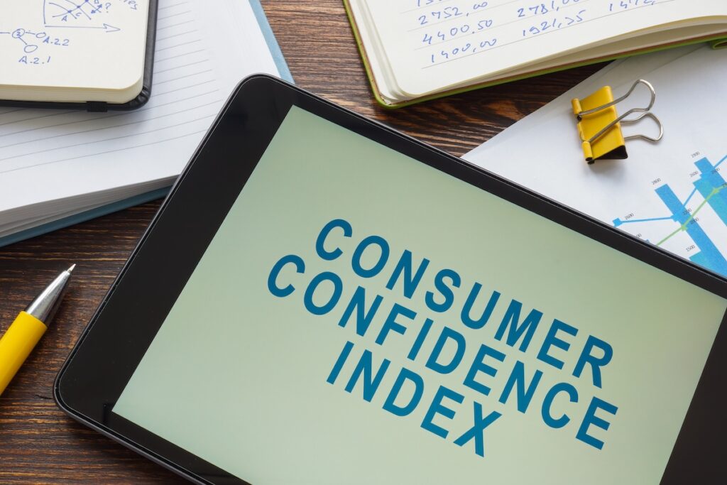 Tablet reading "CONSUMER CONFIDENCE INDEX" next to notepads and data charts